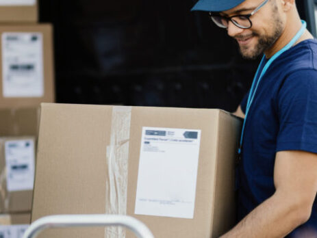 Young happy delivery man carrying cardboard box in a truck.